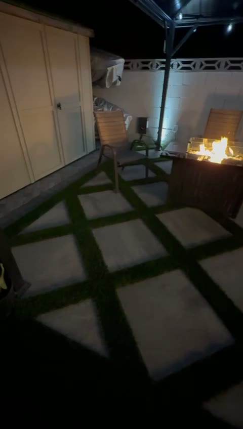 Turf and paver patio lit up at night around a fire pit